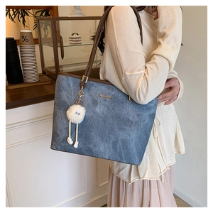 Detail of blue denim tote bag with brown leather handles and a white fuzzy pompom charm