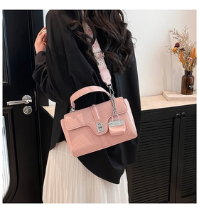Detail der rosa Handtasche mit Krokodilprägung, breitem Jacquard-Gurt und Metallschloss