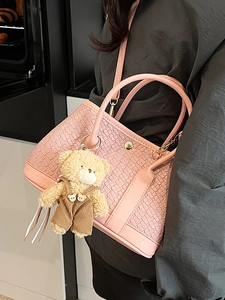 Pink woven bucket handbag for women with cute teddy bear charm on casual model's shoulder