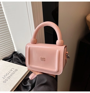 Détail du petit sac à main rose verni avec logo embossé et poignée ronde élégante