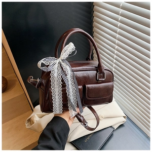 Détail du sac Boston en cuir marron foncé avec nœuds en dentelle et bandoulière réglable