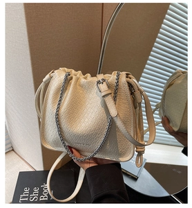 Detail of beige bucket bag with woven texture, metal chain, and adjustable strap