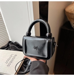 Gros plan d'un sac à main chic en cuir ciré noir poli avec poignée et détails de logo