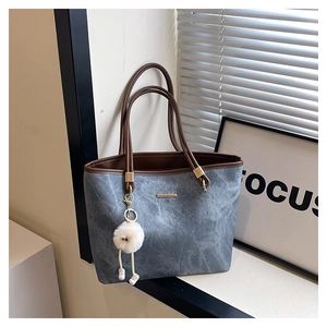 Close-up of a blue tote bag featuring brown straps and a cute plush monster charm