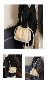 Detail view of cream bucket bag showing woven texture, drawstring closure and silver chain