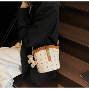 Detail view of cream bucket bag with cartoon bear patterns and leather trim and charms
