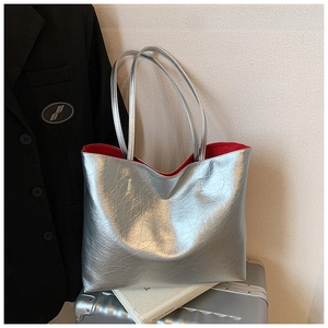 Close-up of silver metallic tote bag with contrasting red lining on a silver suitcase