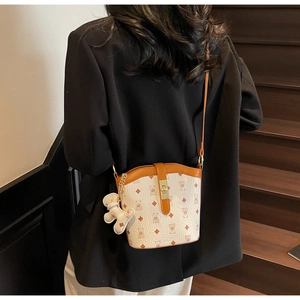 Detail view of printed bucket bag with brown leather trim and bear pendant on a model
