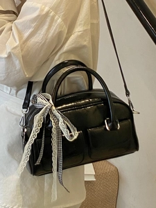 Sac Boston noir brillant avec décoration ruban et doubles poches avant porté par mannequin