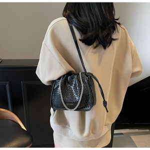 Close-up of black woven bucket bag with silver chain detail on a beige sweatshirt