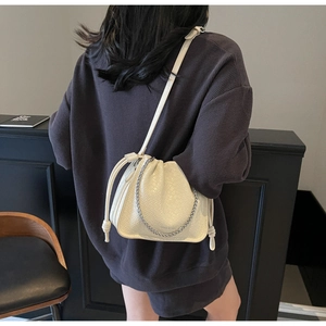 Close-up of beige woven bucket bag with drawstring and silver chain on female model