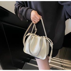 Close-up of beige woven texture bucket bag with silver chain and drawstring detail