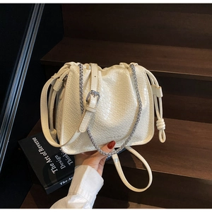 Detail of cream-colored woven bucket bag with silver chain and drawstring closure