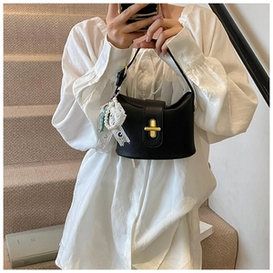 Detail of black lychee-texture bucket bag with gold buckle and pearl lace charm