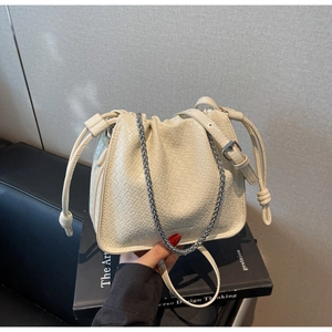 Detail of cream-white woven bucket bag with drawstring closure and silver chain strap