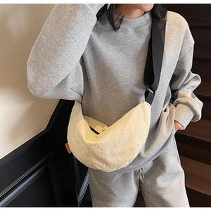 Beige crescent crossbody bag shown in a lifestyle scene with adjustable black strap