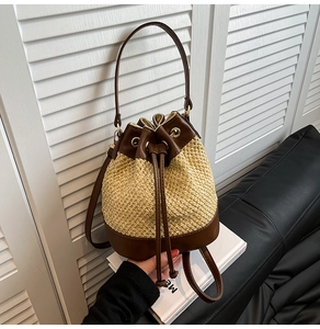 Detail of contrast stitching on woven straw bucket bag with dark brown leather trim