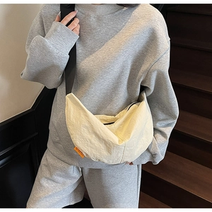 Detail view of beige nylon dumpling bag with orange brand tag and wide black strap