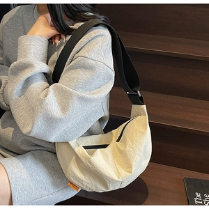 Detail of a creamy nylon crescent bag with a textured finish and black wide strap