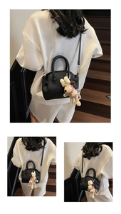 Detail of black lychee grain handbag with beige plush dog charm on a white sweatshirt