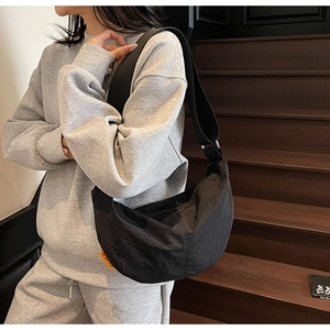 Detail of black nylon dumpling bag featuring a bold orange brand tag and wide shoulder strap