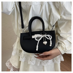 Close-up of black lychee grain bucket bag with pearl bow and silver heart pendant detail