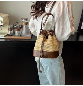 Detail view of woven straw bucket bag with contrast leather trim and drawstring closure