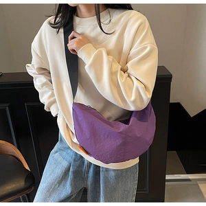 Detailed close-up of a purple nylon dumpling bag with orange tag and wide black shoulder strap