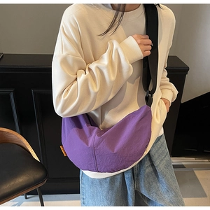Close-up of purple crescent crossbody bag with orange side label and wide strap
