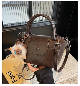Detail of a dark brown vintage handbag featuring a cute white alpaca plush charm accessory