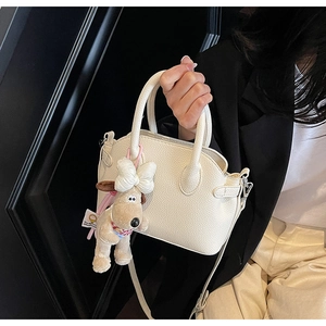 Close-up of white lychee pattern leather bag with a cute plush dog charm hanging on handle