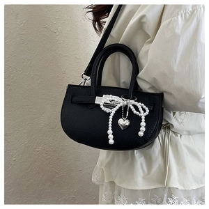 Detail of black leather bucket bag with pearl bow and silver heart charm decoration