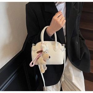 Detail of white lychee texture leather shell bag with cute plush puppy charm accessory