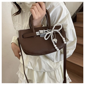 Detail of dark brown lychee leather bucket bag with pearl bow and silver heart pendant