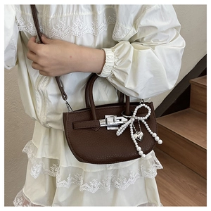 Close-up of dark brown lychee leather handbag with pearl bow and silver twist lock detail
