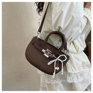 Detail of dark brown lychee leather bucket bag with silver lock and pearl bow charm