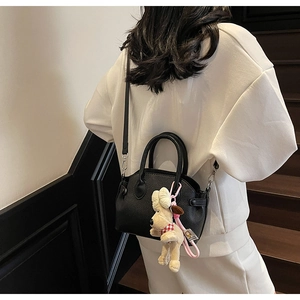 Detailed back view of a black litchi pattern shell bag with white puppy plush pendant