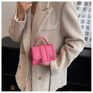 Détail du mini sac rose vif avec gaufrage crocodile et chaîne argentée sur blazer clair