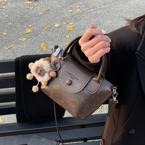 Détail d'un sac à main vintage marron foncé avec charme en peluche sur un banc en bois