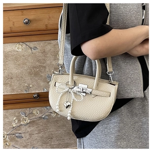 Close-up of beige lychee texture leather bucket bag with pearl bow and heart pendant detail