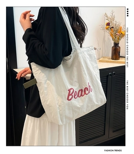 Detail of white nylon tote bag with red Beach typography and green ribbon strap