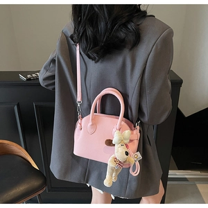 Pink litchi texture shell bag with dog plush charm shown on person for size reference