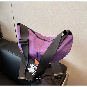 Close-up of purple nylon crescent bag featuring a black wide strap and orange side label