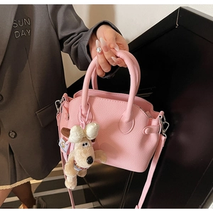 Detail of pink litchi grain shell bag featuring a cute plush dog pendant and metal buckle