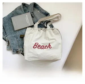 Flat lay of a white drawstring tote bag with red Beach text and denim jacket