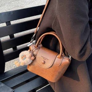 Détail d'un sac à main rétro en cuir marron avec un élégant pompon décoratif.