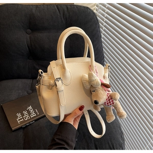Detail of cream lychee leather handbag featuring a cute plush dog charm and crossbody strap