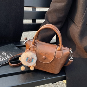 Détail d'un sac à main en cuir marron avec logo embossé et breloque peluche animal