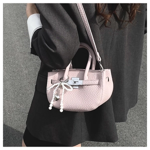 Detail of pink lychee leather bucket bag with silver turn-lock and pearl bow charm