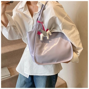 Close-up of lilac glossy shoulder bag featuring a white pegasus charm on a female model